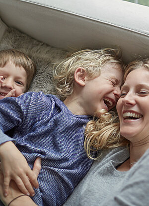 Eine Frau liegt mit ihren beiden Kindern auf der Couch